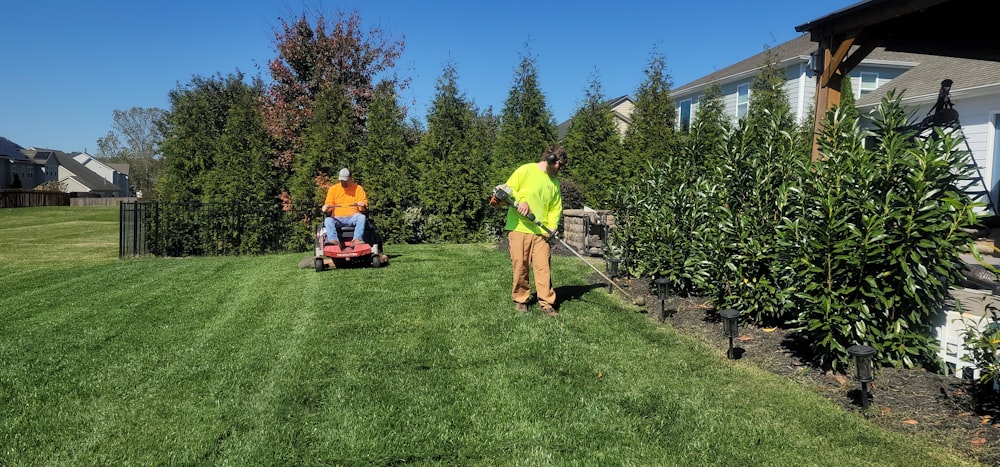 Two crew members mowing and trimming a fenced backyard lawn with fresh mow lines