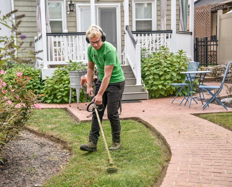 Crew member string-trimming a lawn edge along a brick garden path